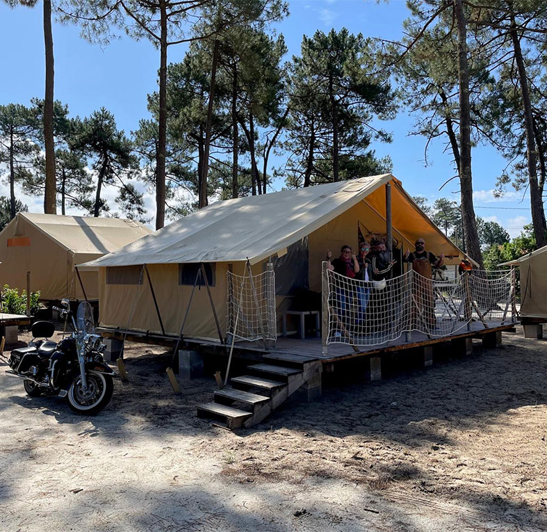 Vue extérieure d’une tente lodge, équipée d’une terrasse en bois. Hébergement insolite en Gironde au camping Montacabana à Montalivet